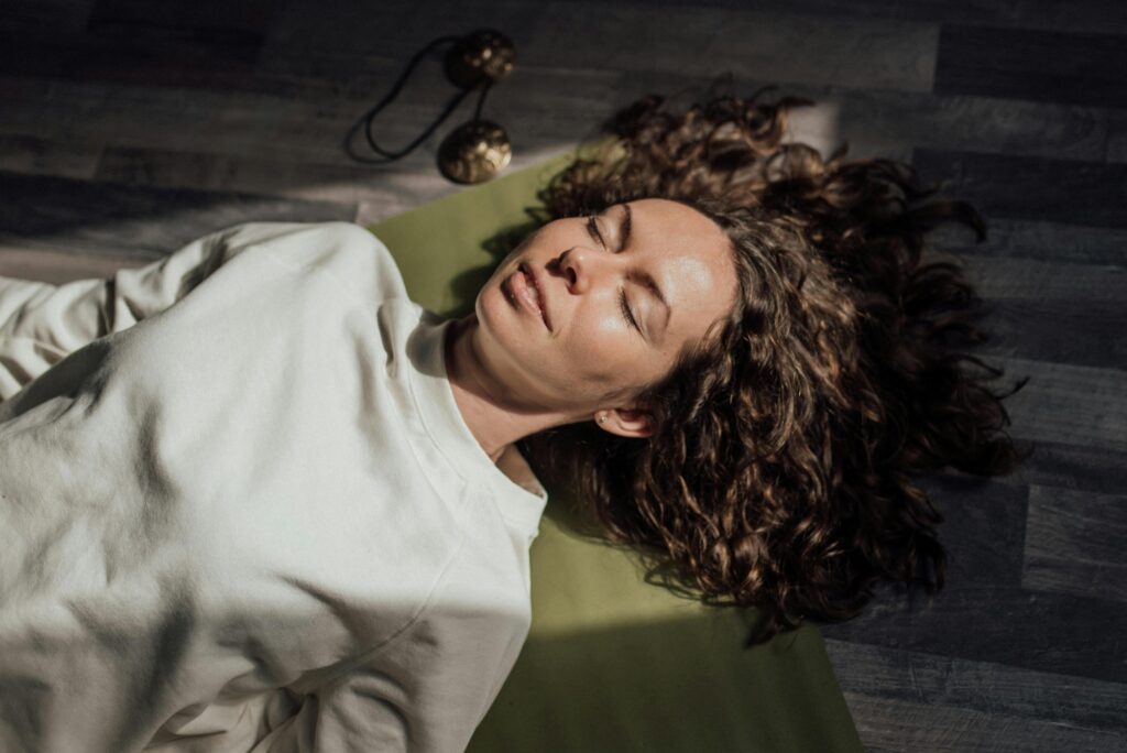 Woman with curly hair meditating on yoga mat indoors, eyes closed.