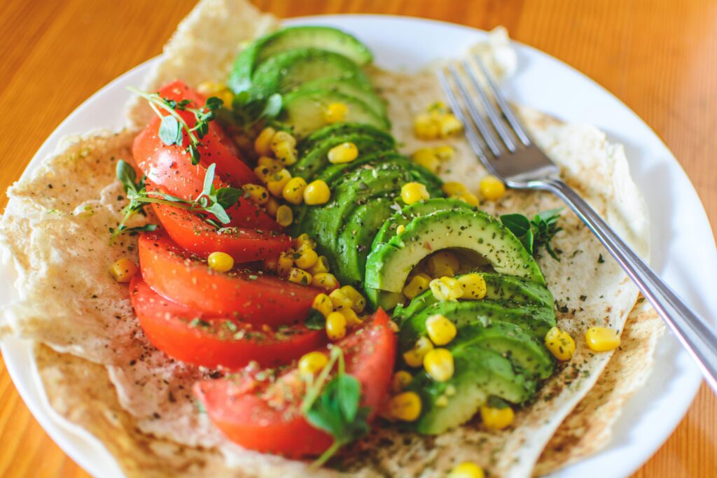 A vibrant salad with avocado, tomato, and corn on flatbread, topped with herbs, perfect for a healthy meal.